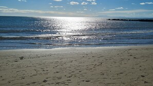 Une plage où l’on peut voir des empreintes dans le sable, un ciel dégagé et le soleil qui se reflète sur l’eau.