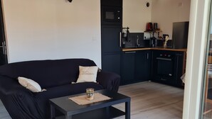 Una sala de estar moderna con un sofá negro, una mesa de centro y una zona de cocina con electrodomésticos.