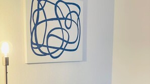Un salon moderne avec un canapé gris, des coussins décoratifs jaunes et bleus, une lampe sur pied et une œuvre d’art abstraite accrochée au mur.