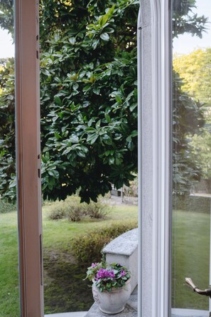 A window with a view of a lush green garden and a potted plant with purple flowers. - Villa Dell Artista by Elite Villas (Cernobbio)