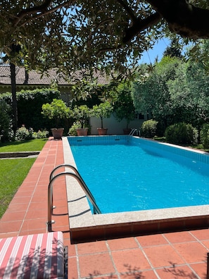 Ein rechteckiger Pool mit einer gefliesten Kante, umgeben von einem Pflasterweg und Blumentöpfen.