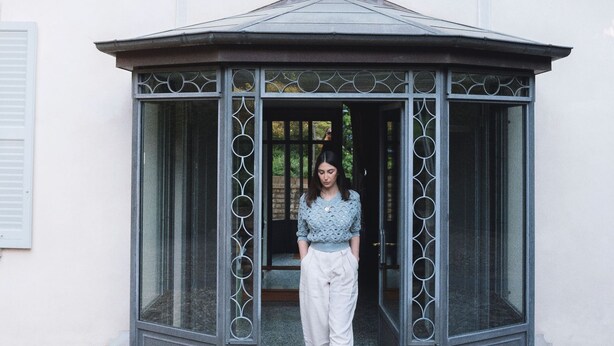 A woman standing in a glass-walled gazebo with a tiled floor, next to a building with white walls and shutters. - Villa Dell Artista by Elite Villas (Cernobbio)
