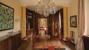 A dining room with a long wooden table, red chairs, a chandelier, and a view into a living area. - Villa Dell Artista by Elite Villas (Cernobbio)
