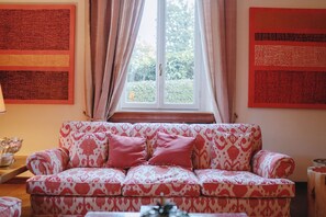Un salon avec un canapé à motifs, une fenêtre avec des rideaux et un mur recouvert de panneaux rouges.