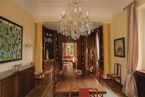 A dining room with a long wooden table, red chairs, a chandelier, and a view into a living area. - Villa Dell Artista by Elite Villas (Cernobbio)