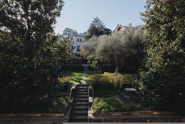 Un escalier en pierre mène à un bâtiment entouré d’une végétation luxuriante et d’arbres.