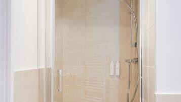 Une cabine de douche fermée par des parois en verre, dotée d’un pommeau de douche à main et d’un robinet fixé au mur.