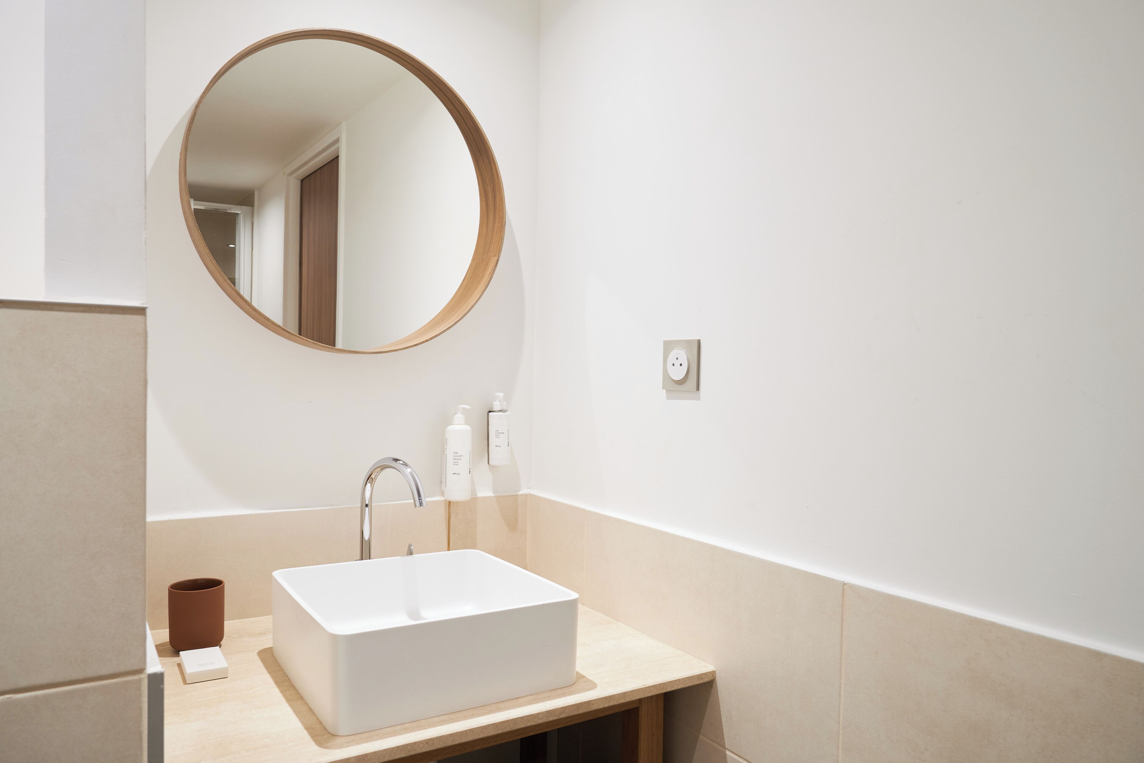A bathroom with a white sink, a round mirror, and a towel rack.
