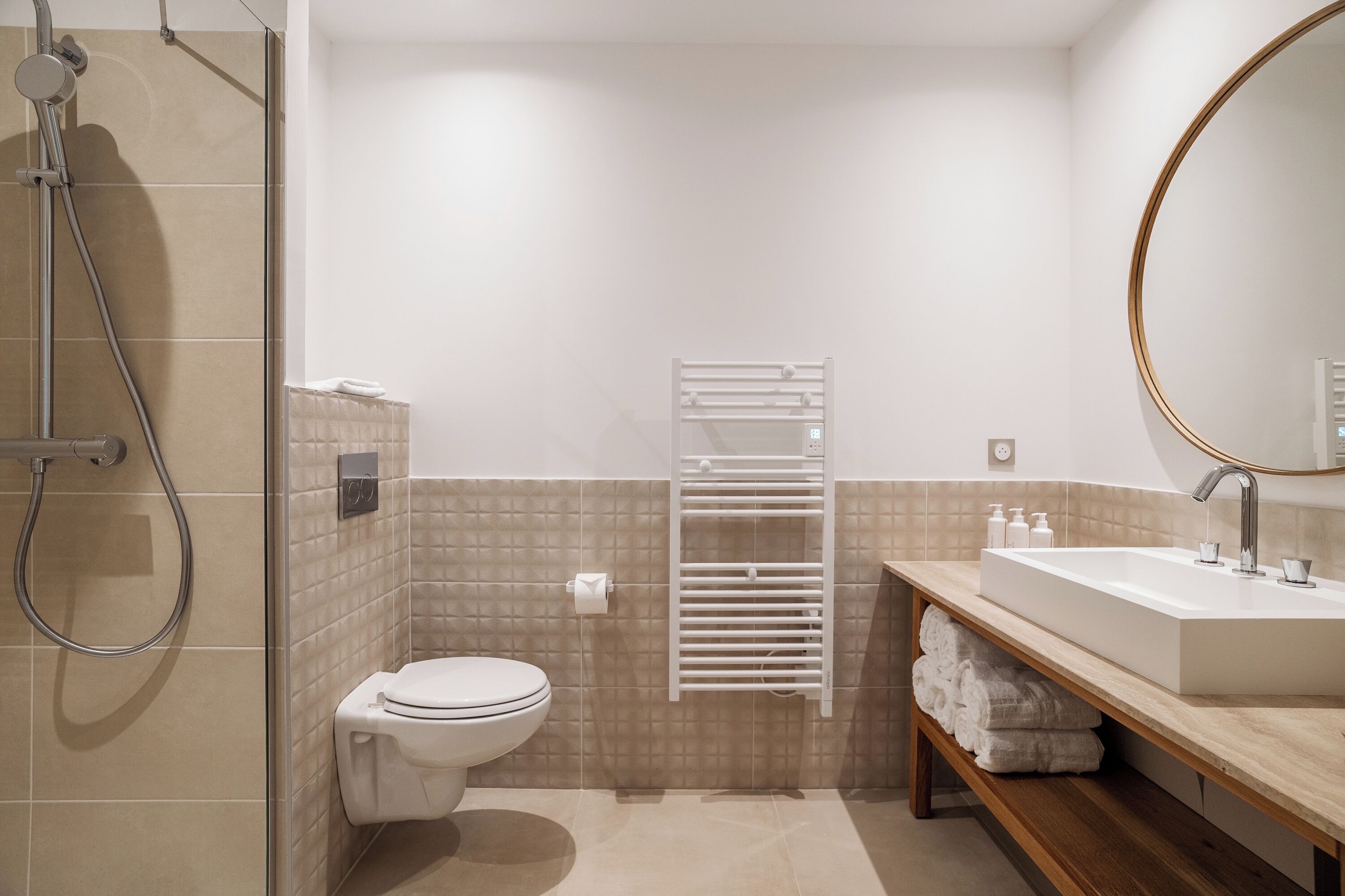 Un baño moderno con ducha, inodoro, toallero y lavamanos con artículos de aseo.