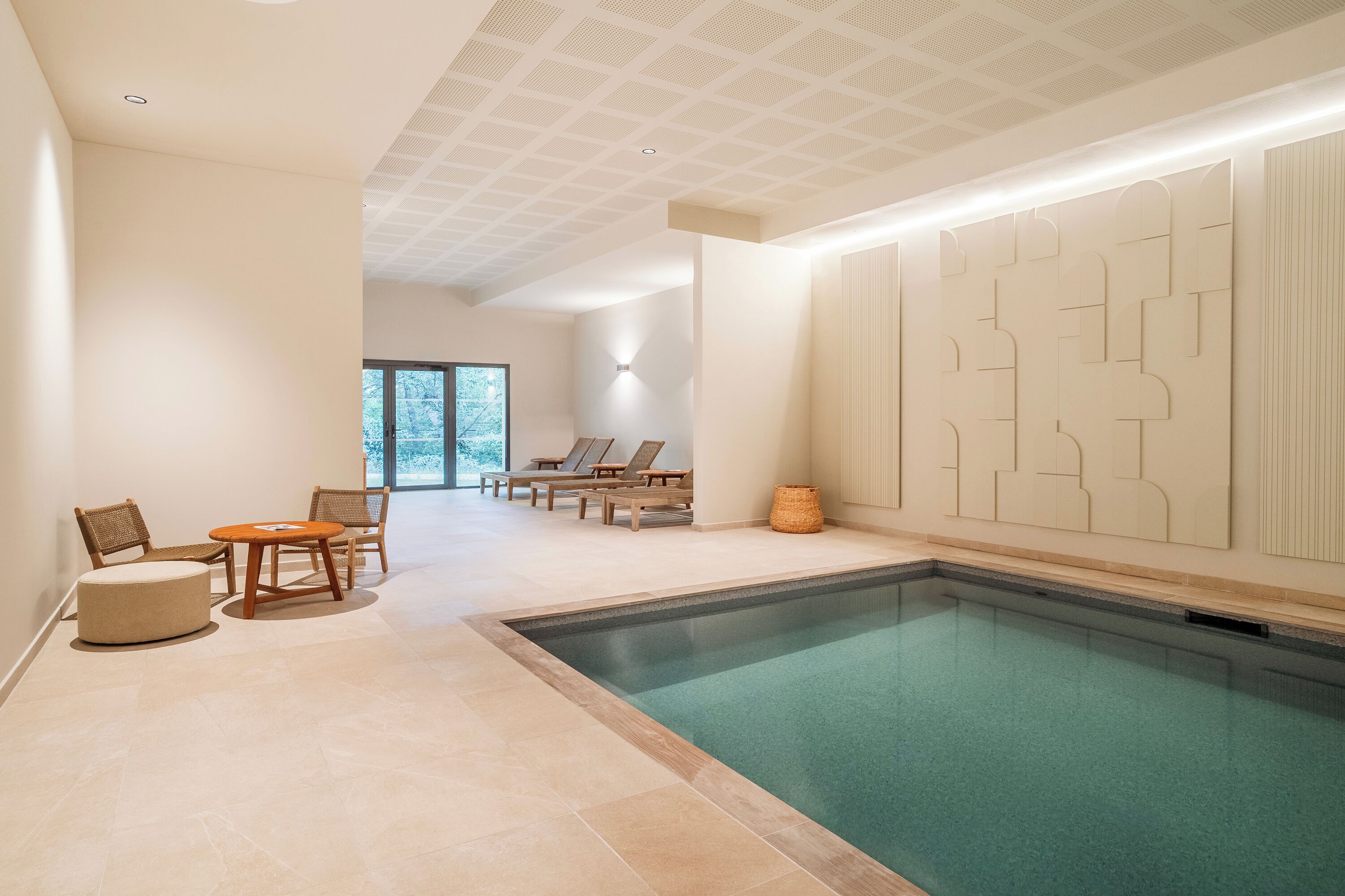 Un espace piscine doté de chaises longues et d’un mur orné de motifs géométriques.