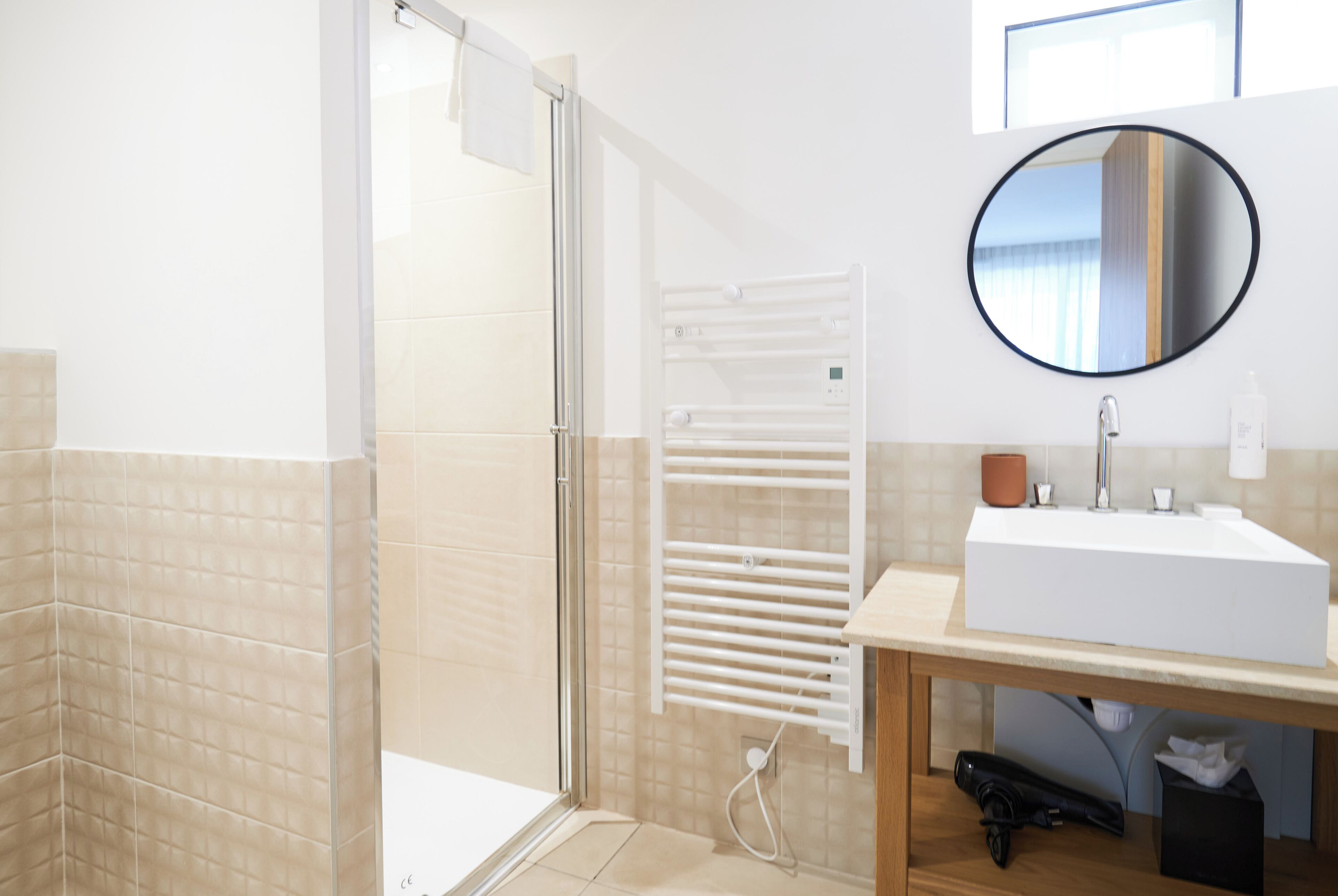 Un baño moderno con cabina de ducha de vidrio, un lavabo blanco y un espejo redondo en la pared.