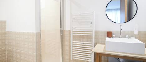 A modern bathroom with a glass shower enclosure, a white sink, and a round mirror on the wall.