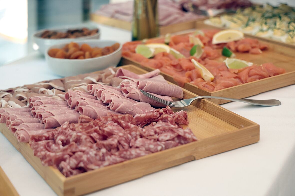 A variety of meats arranged on wooden boards, including sliced and rolled options, with a spoon and fork placed on the board.