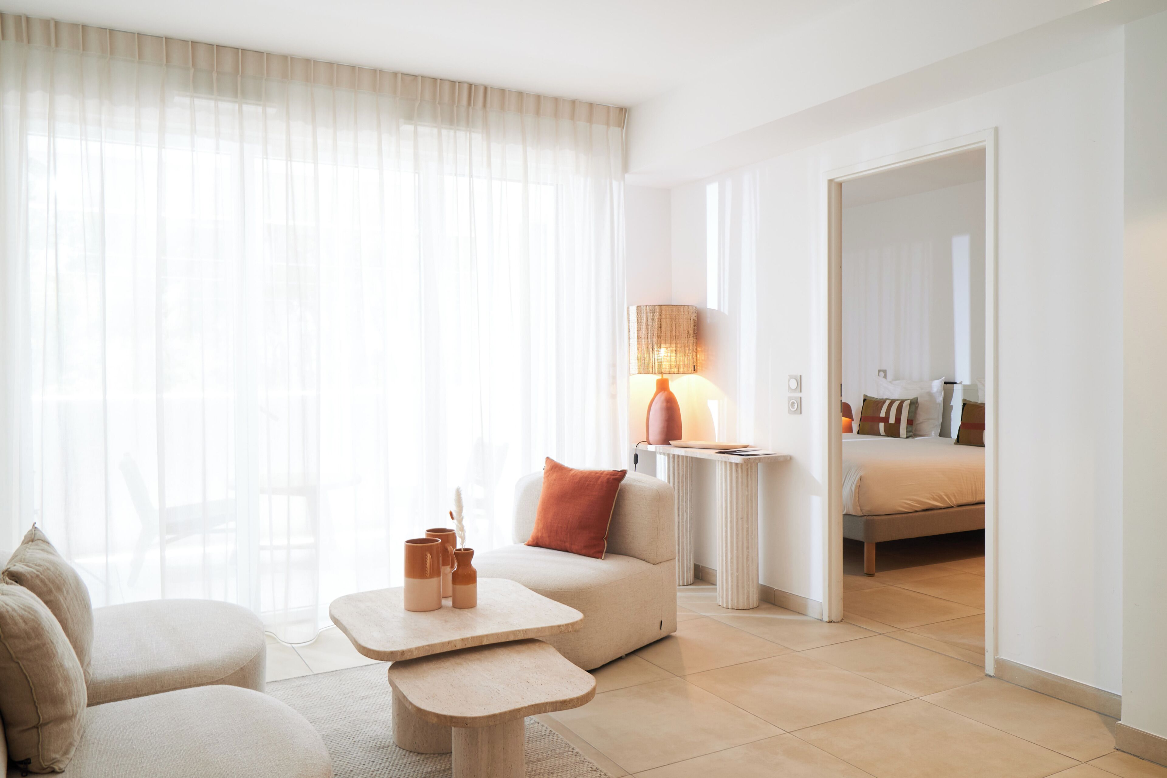 Quarto de hotel com sofá, uma mesinha, luminária e cama.