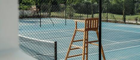 Tenniskenttä, jossa on puinen tuoli ja verkko.