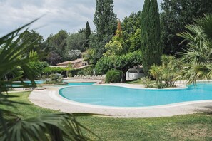A large, curved swimming pool surrounded by lush greenery and tall trees. - SetClub Hôtel & Spa (Aix-en-Provence)