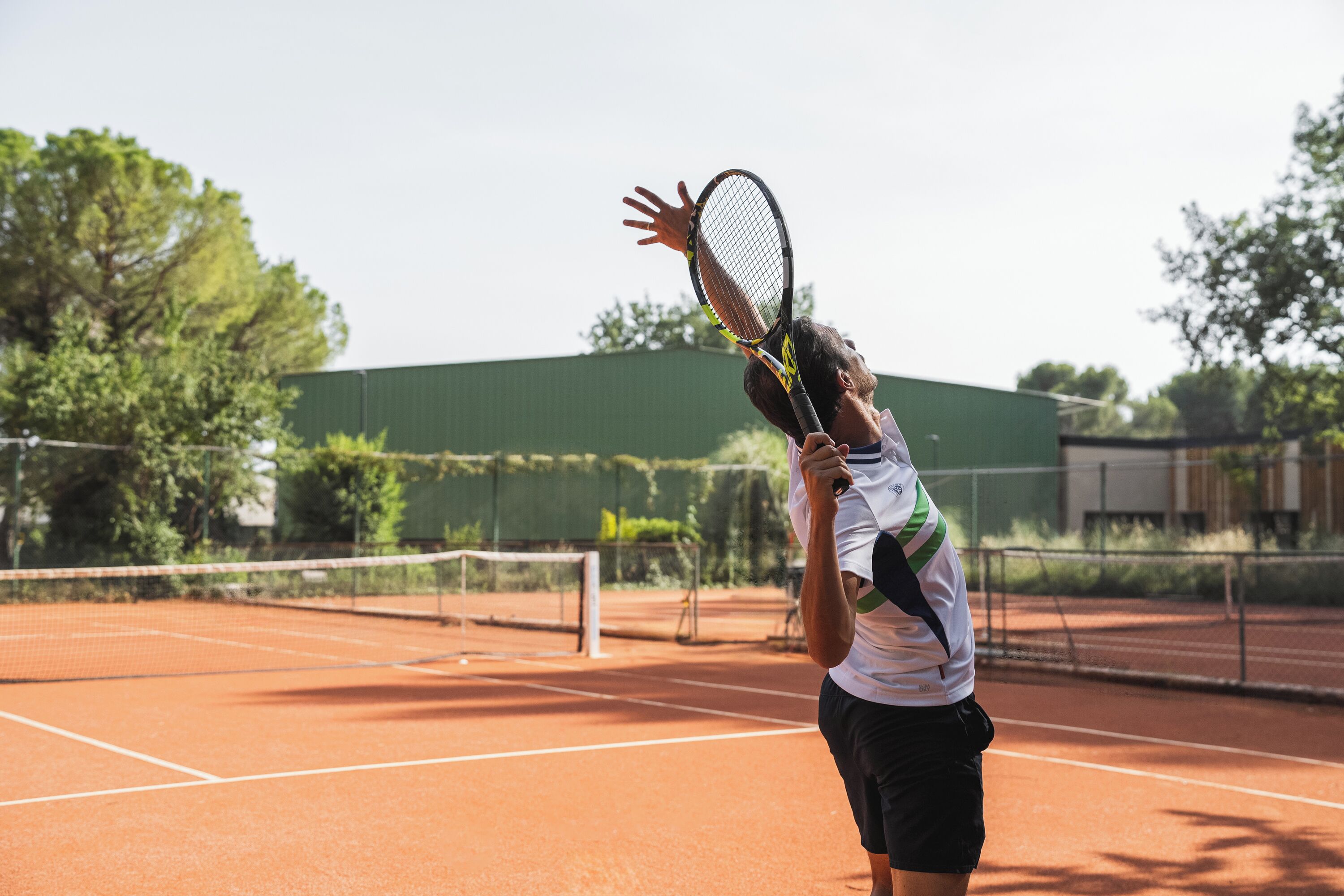 Un court de tennis avec un filet, une clôture verte et des arbres en arrière-plan.