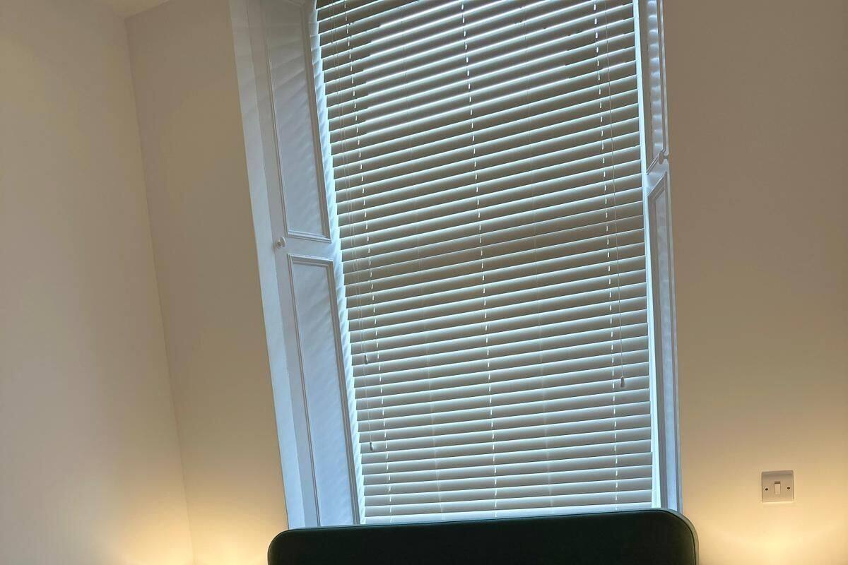 A neatly made bed with white linens, two bedside lamps, and a window with blinds.