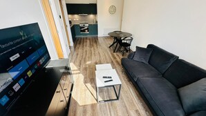 Una sala moderna con televisor, sofá, mesa de centro y una zona de comedor con mesa y sillas.
