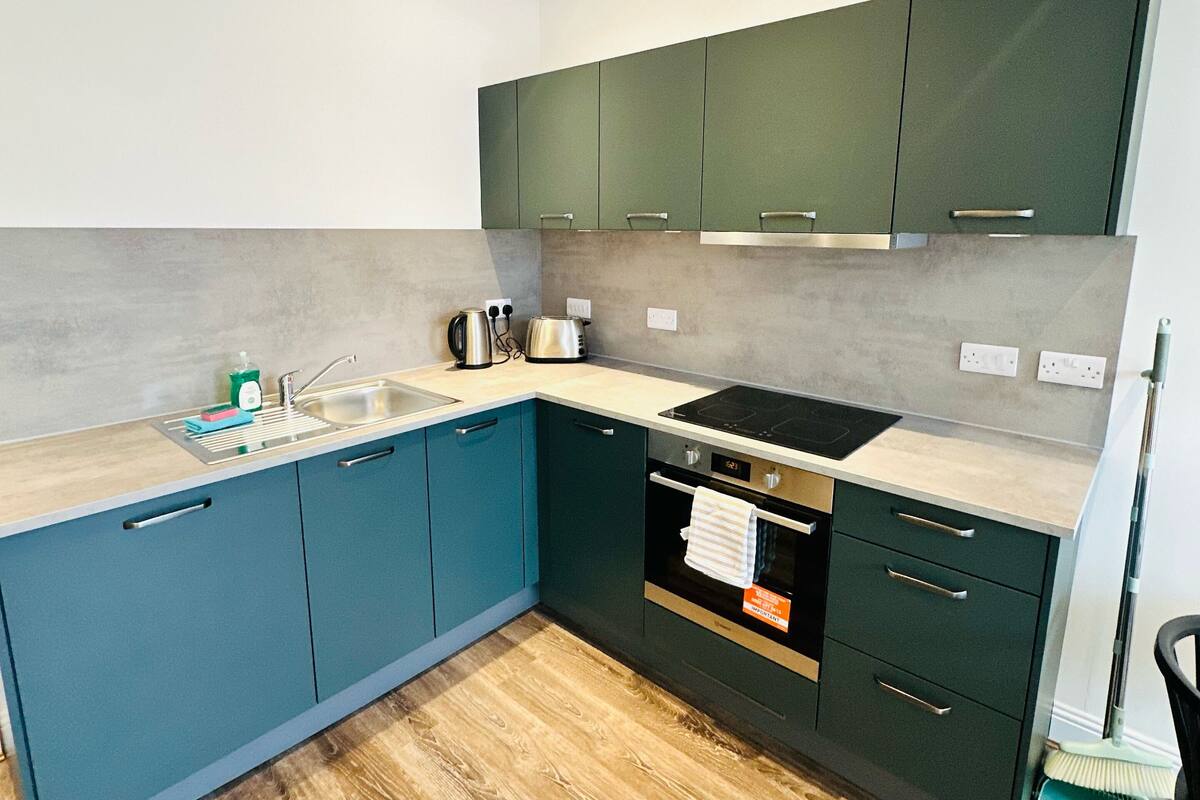A modern kitchen with teal cabinets, a wooden floor, and a built-in oven.