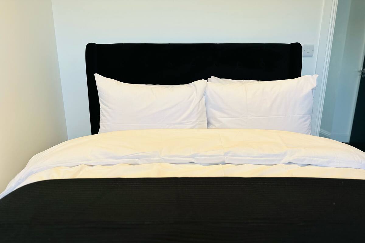 A bed with a black headboard, white pillows, and a white bedspread.