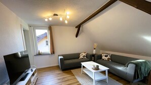 Uma sala de estar moderna com televisão de tela plana, sofás cinzas, uma mesa de centro branca e piso de madeira.