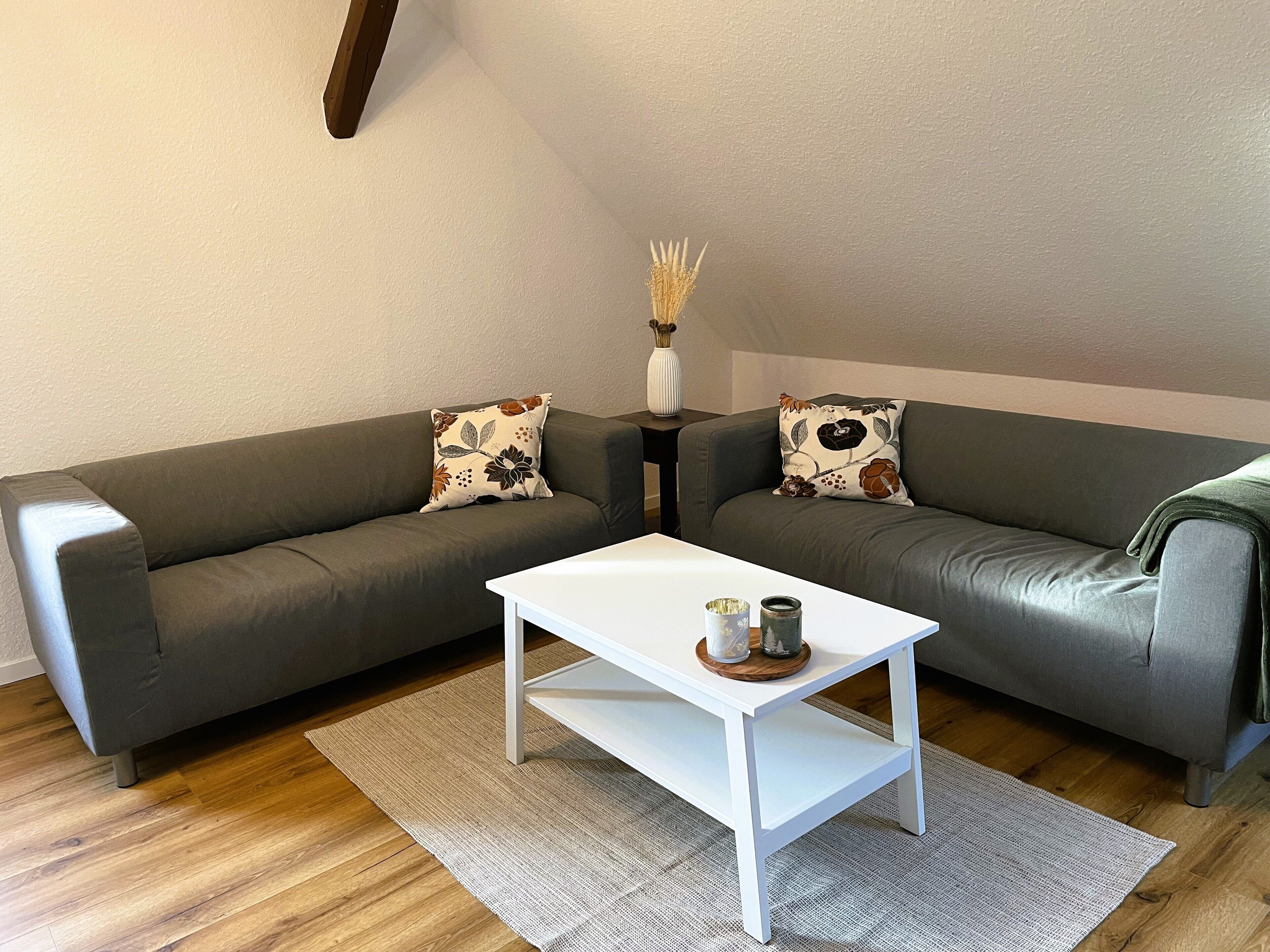 Ein Wohnzimmer mit zwei grauen Sofas, einem weißen Couchtisch und einem Teppich mit Muster.