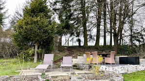 Área de jardim com mobiliário para área externa, vasos de pedra e um pano de fundo de árvores.