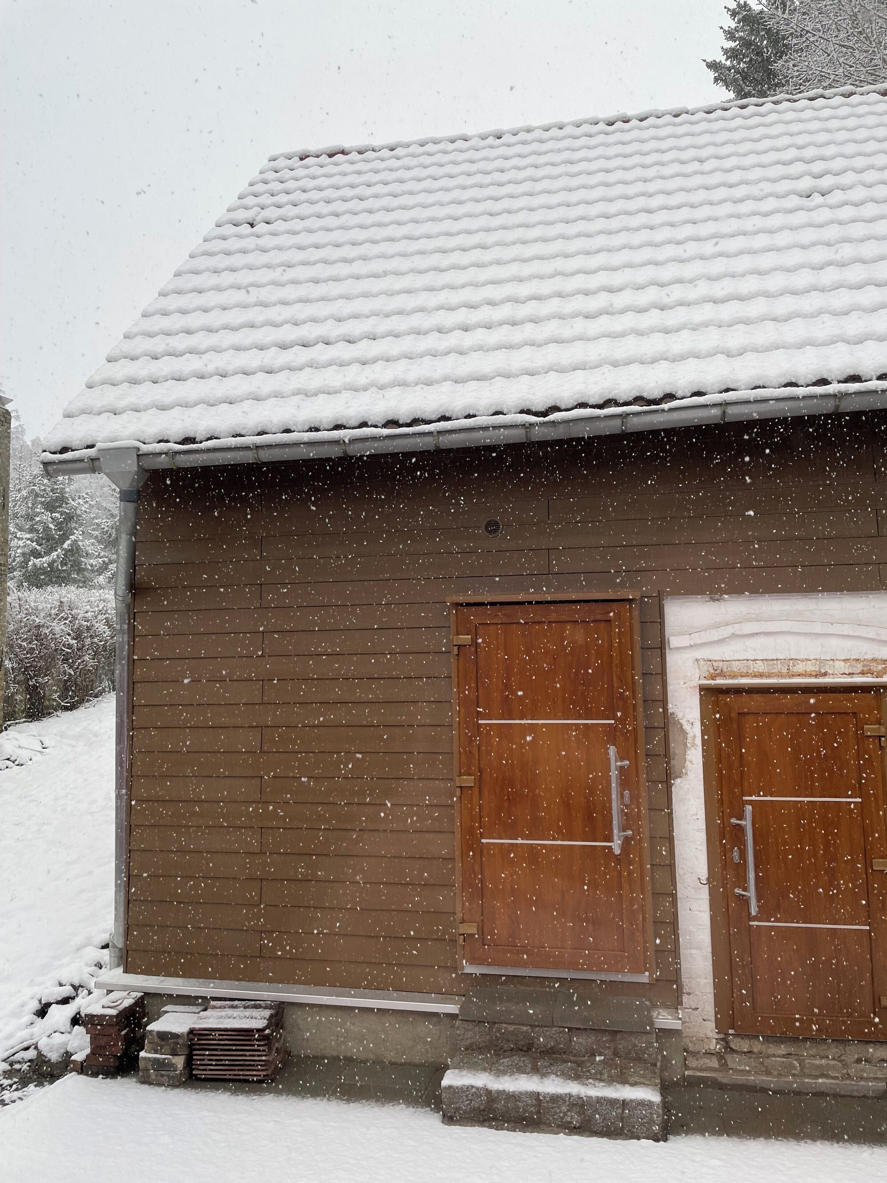 A wooden building with a snow-covered roof and two wooden doors.
