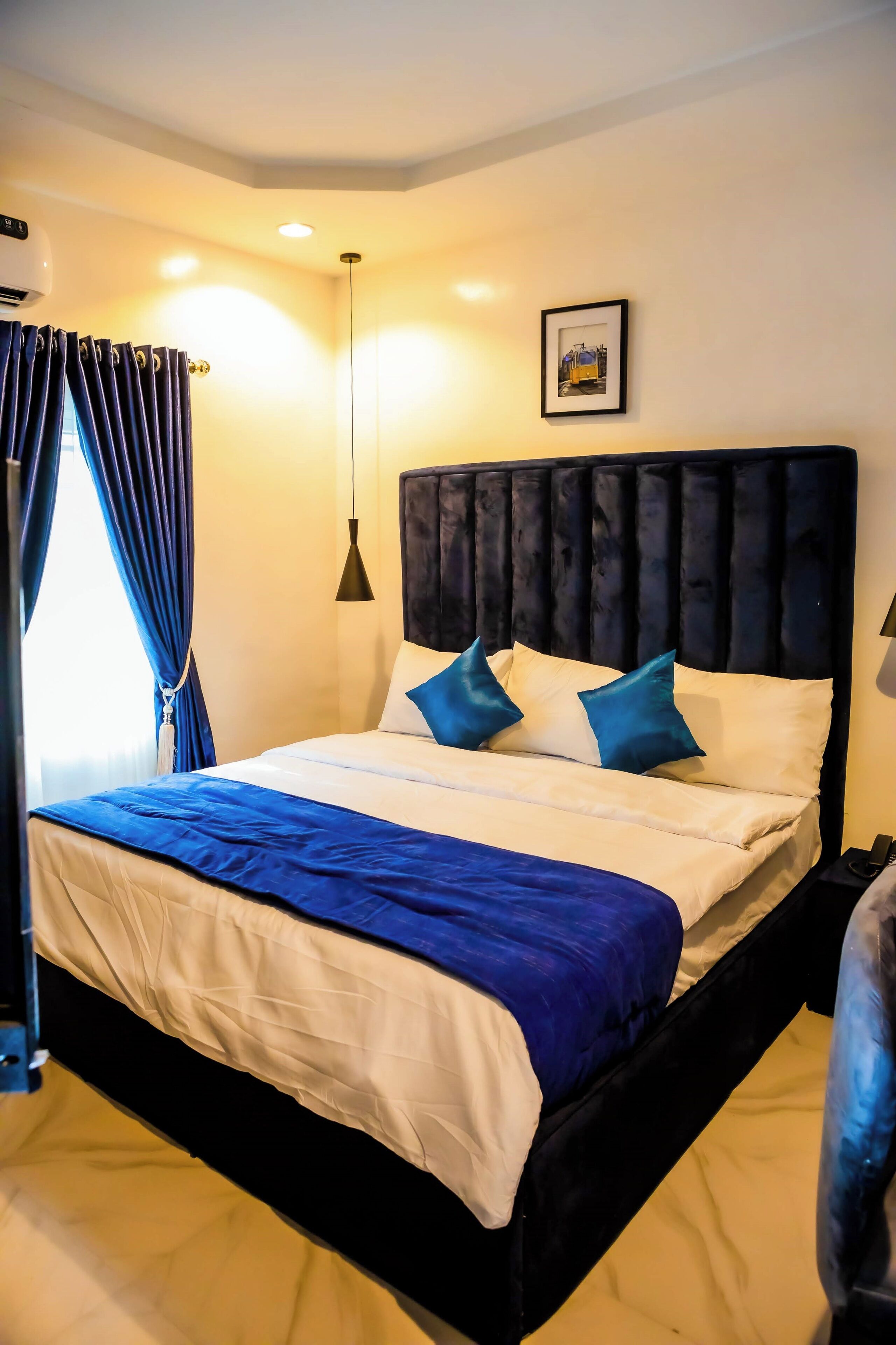 A neatly made bed with a blue and white bedspread, a dark headboard, and two pillows.