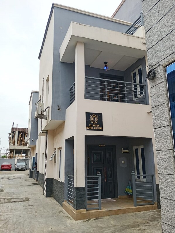A two-story hotel with a balcony on the upper floor, a sign indicating it is El Elyon Hotel & Suites, and a gated entrance. - El Elyon Hotel and Suites (Lagos)