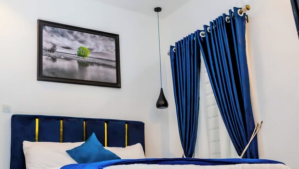 Una cama bien hecha con un cabecero azul, ropa de cama blanca y una manta azul y blanca.