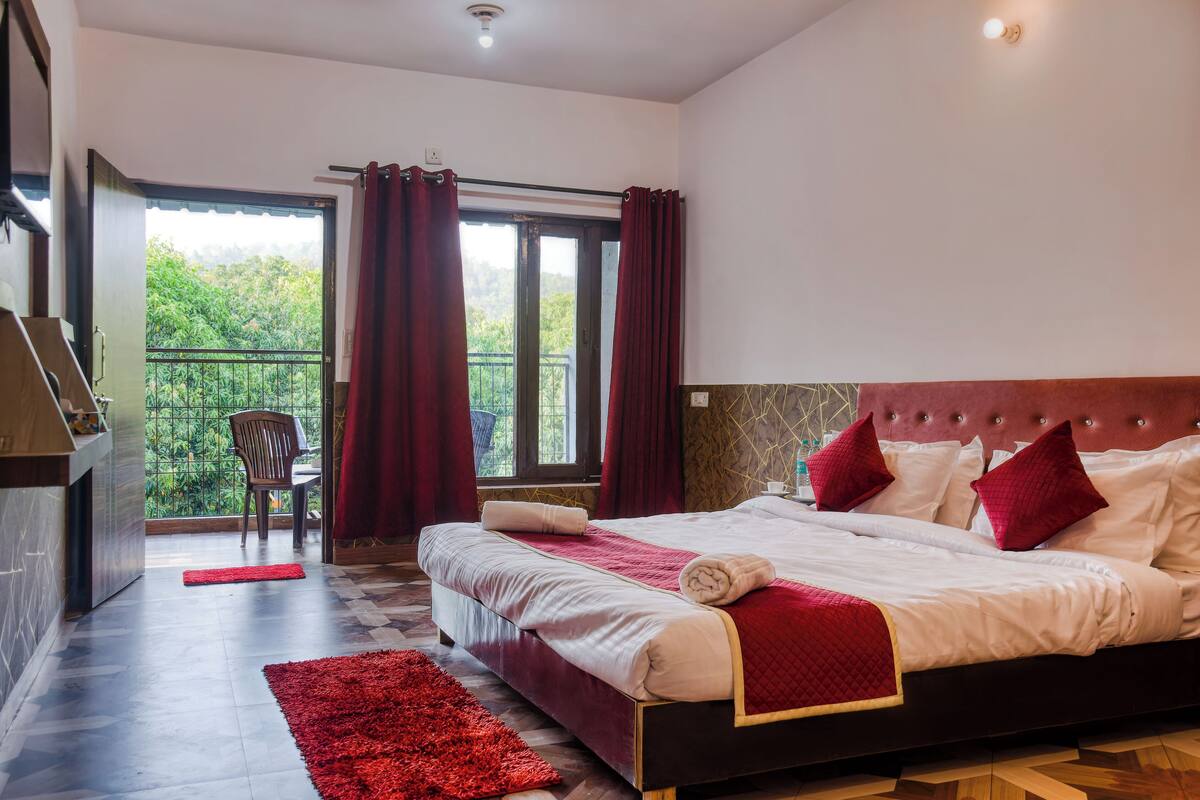 A bedroom with a large bed, a balcony with a chair, and a view of greenery.