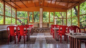 A covered dining area with red chairs and tables, large windows, and a stone wall.