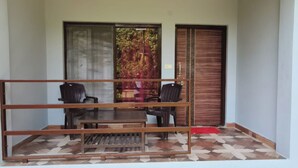 A balcony with a wooden table and two chairs, a sliding glass door, and a patterned floor.