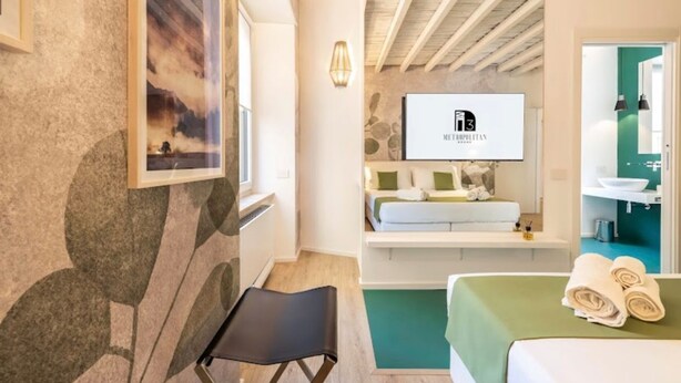 A hotel room with a bed, a seating area, a television, and a bathroom visible through an open door. - Metropolitan Rooms (Cagliari)