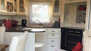 A compact kitchen with white cabinets, a central island, a black stove, and a red trash bin. - Beautiful 2-bed Chalet in Llanfairpwllgwyngyll (Llanfairpwllgwyngyll)