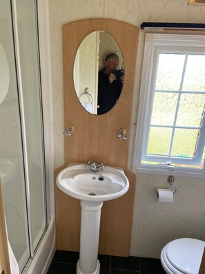 A bathroom with a pedestal sink, a wooden door with a mirror, a toilet, and a window with patterned glass. - Beautiful 2-bed Chalet in Llanfairpwllgwyngyll (Llanfairpwllgwyngyll)
