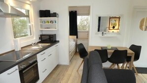 Eine kleine Küche mit Herd, Spüle und Schränken, ein Essbereich mit Tisch und Stühlen sowie eine Sitzecke mit einer Couch.
