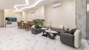 A modern hotel lobby with a marble floor, a dining area with chairs and a table, a sofa, and a TV. - V'Luna Hotel Can Tho (Can Tho)