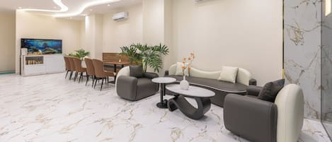 Un moderno vestíbulo de hotel con piso de mármol, un comedor con sillas y una mesa, un sofá y un televisor.