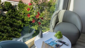 A modern room with a round white table, a comfortable chair, a vase with red flowers, and a view of greenery outside. - V'Luna Hotel Can Tho (Can Tho)
