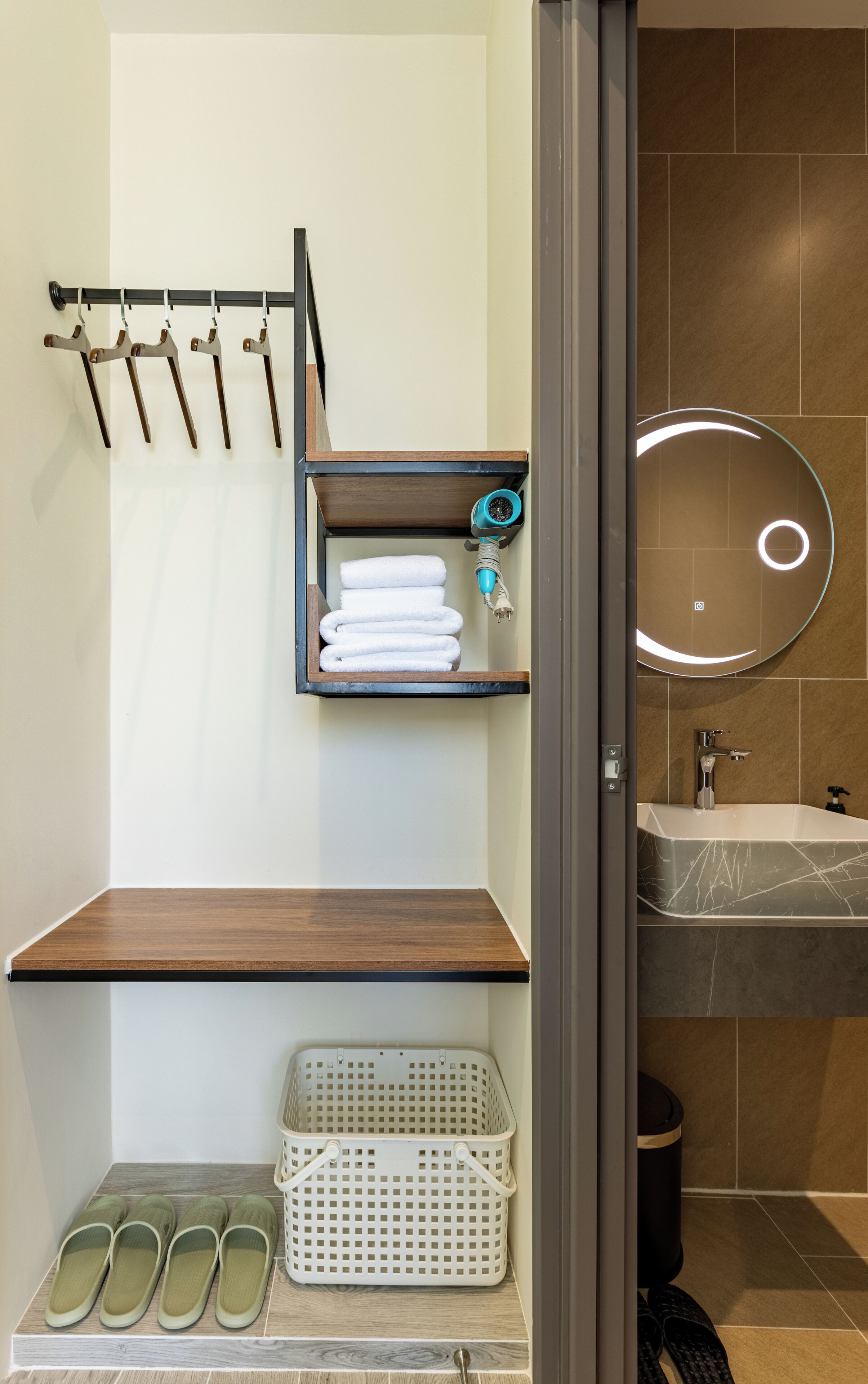 A bathroom with a wooden shelf holding towels, a hanging rack, a laundry basket, and a sink with a marble countertop.