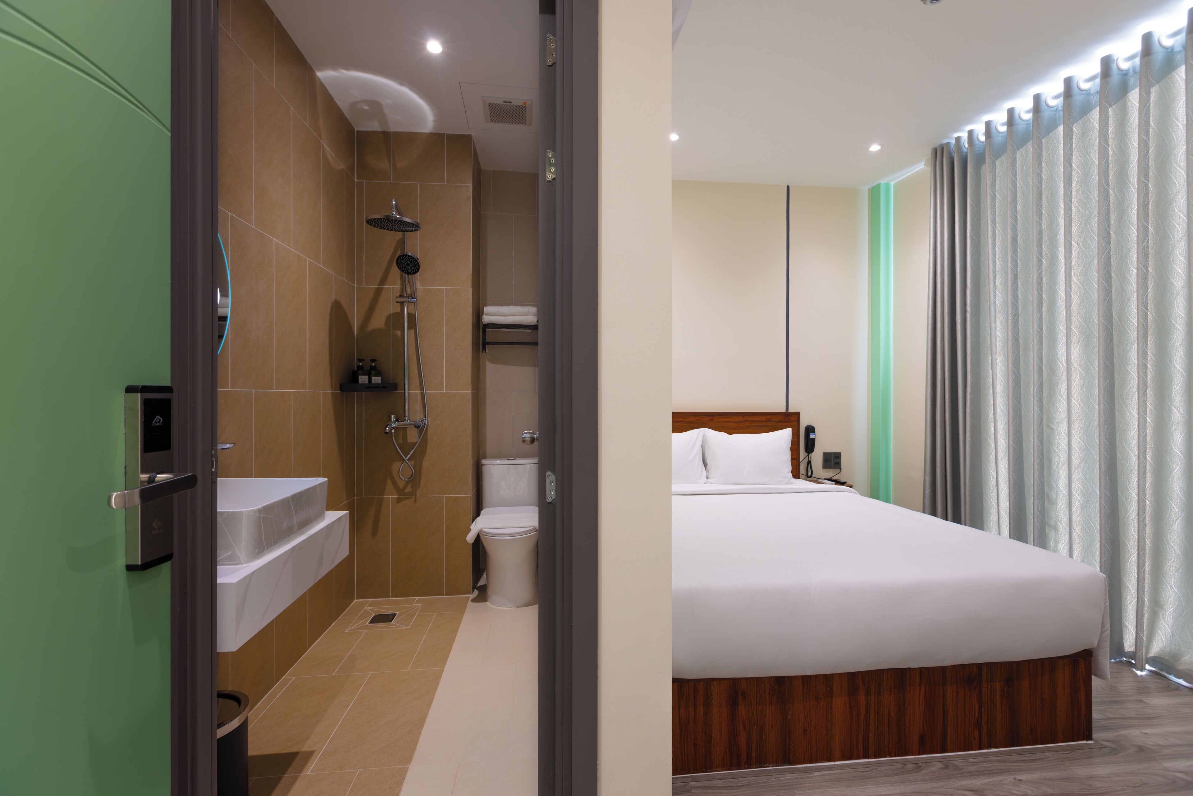 A hotel room with a shower, toilet, sink, and a bed with a wooden headboard.
