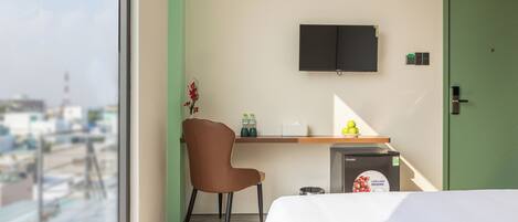 A hotel room with a bed, a desk with a chair, a television, and a view of the cityscape.