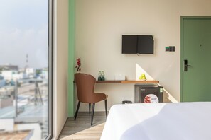 Una habitación de hotel con cama, escritorio, silla, televisión y vista a la ciudad.