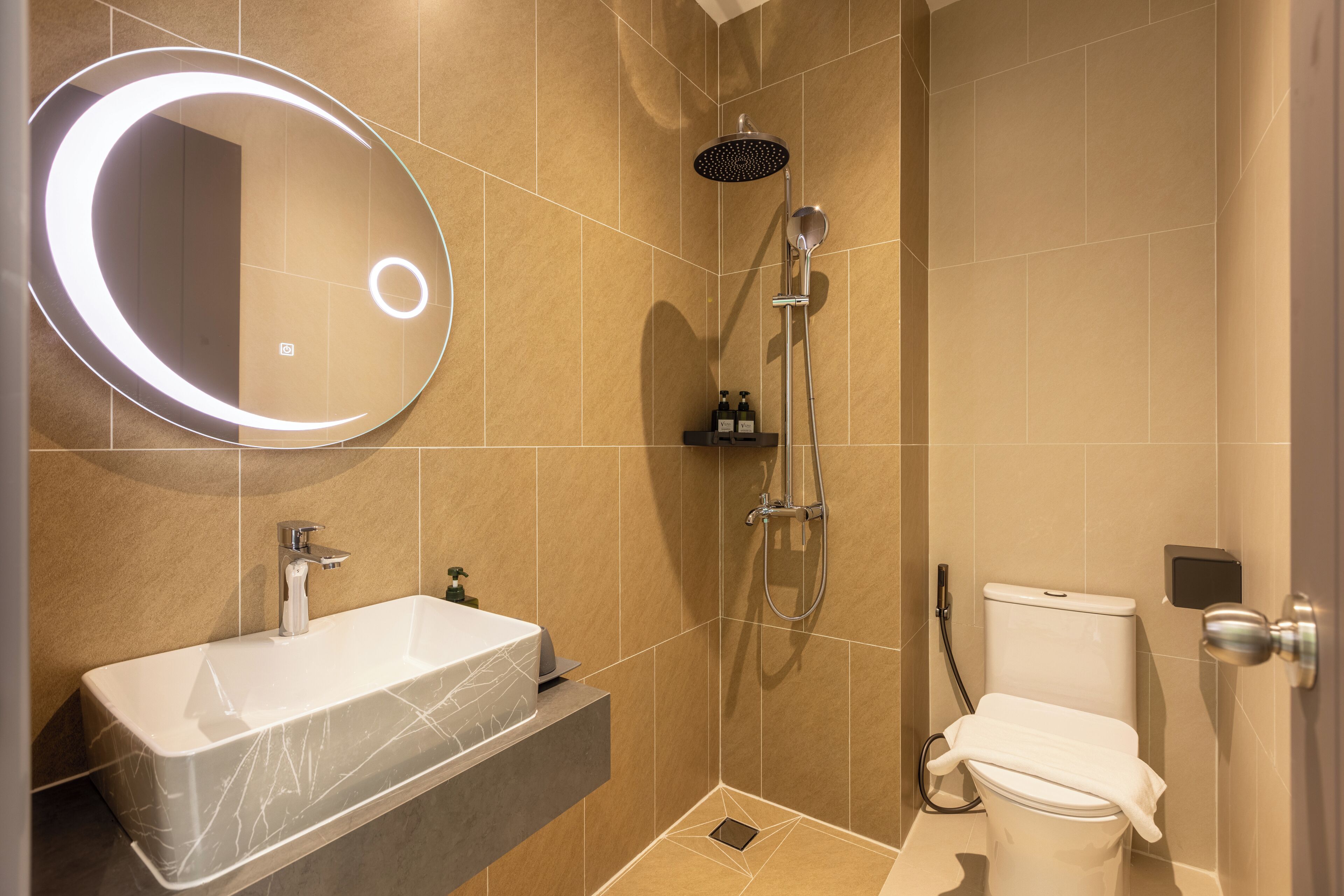 Un baño moderno con lavamanos de mármol, un espejo redondo, ducha de mano e inodoro.