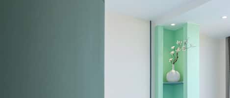 A hotel room with a bed, a green wall, and a white vase with flowers.