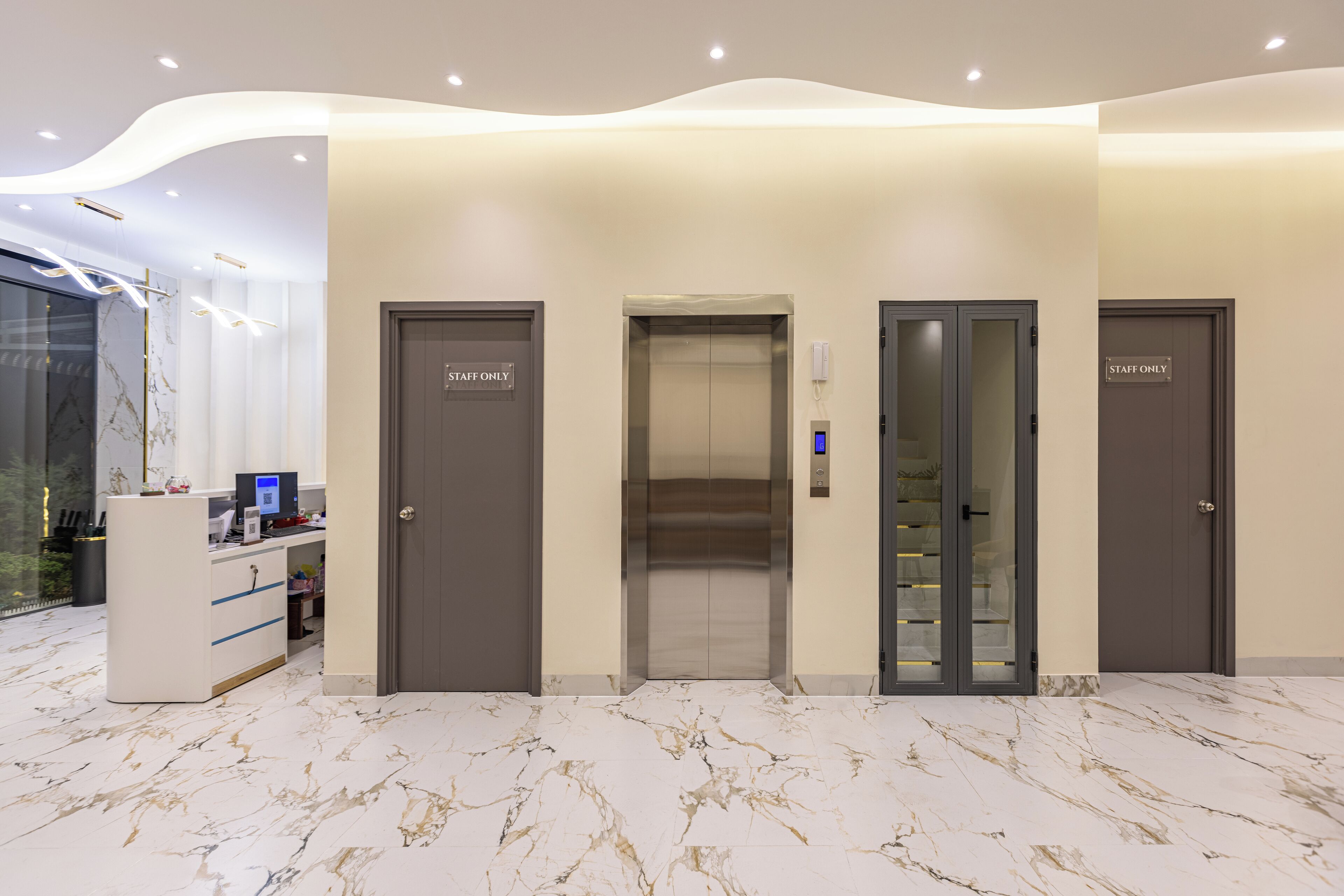 A modern hotel lobby with marble flooring, a reception desk, and three elevator doors labeled "STAFF ONLY".