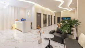 A modern reception area with a marble floor, a reception desk, a sofa, and a large potted plant. - V'Luna Hotel Can Tho (Can Tho)